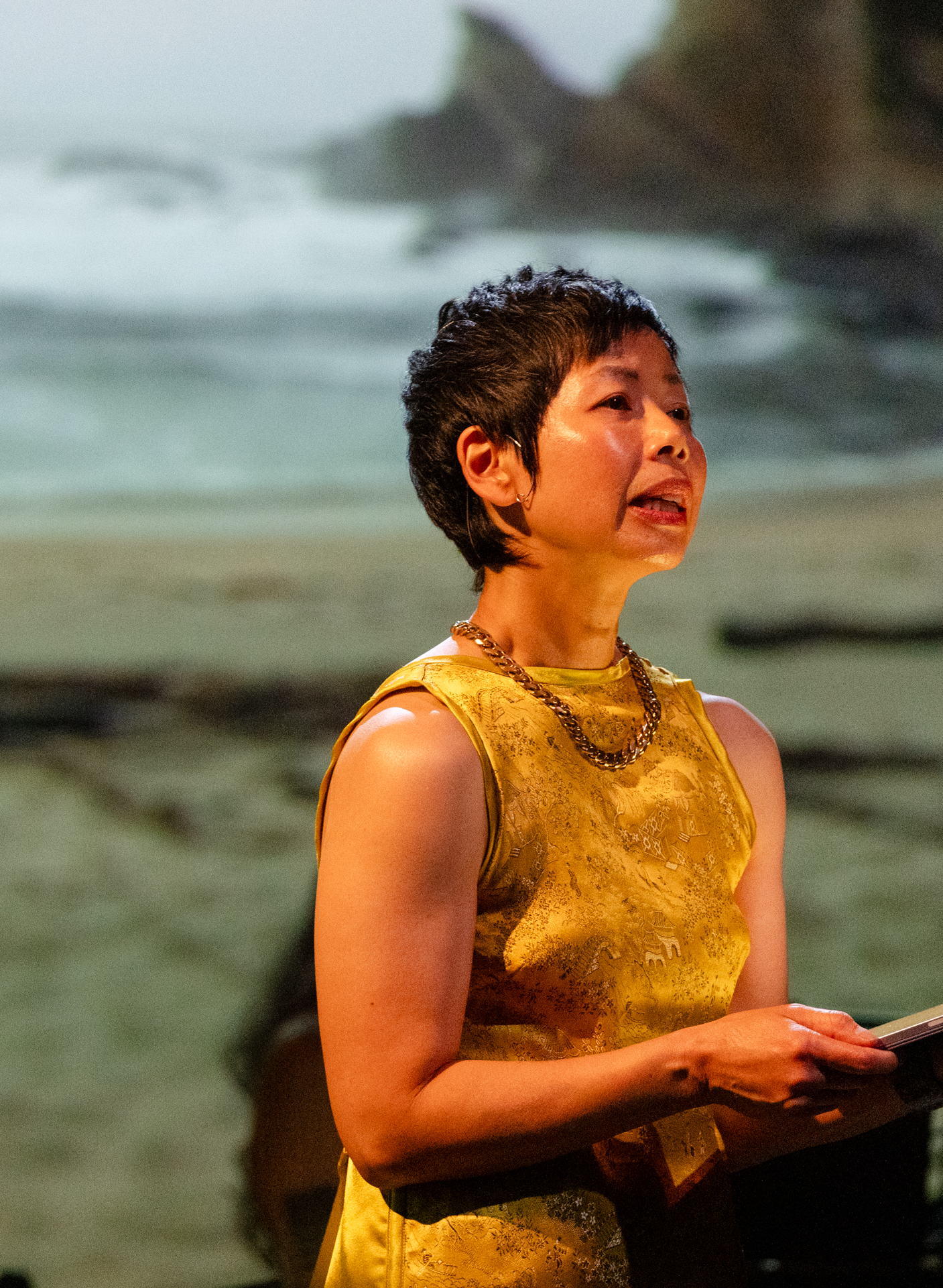 short-haired Asian woman in a gold dress speaking