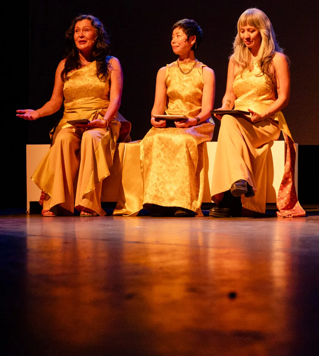 Hoa Nguyen, Barbara Tran, Dao Strom, all dressed in yellow on a dark stage